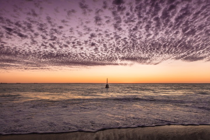 Vibrant sunset over ocean with purple clouds and a lone buoy in the water.