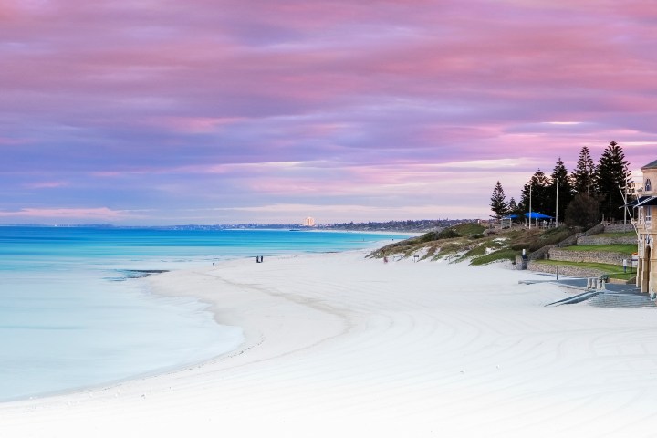 Beach with a historic building, pink sky, and calm ocean at sunset.
