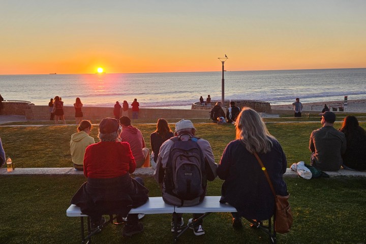 People sitting on benches watching the sunset over the ocean.
