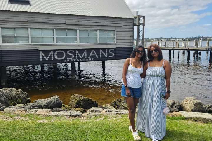 Two people posing in front of Mosmans Restaurant by a waterfront.