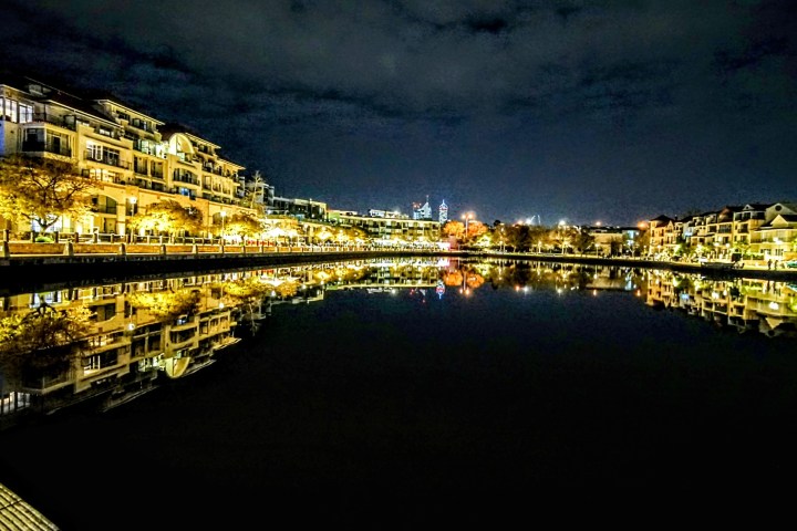 Night view of illuminated waterfront buildings reflecting in calm water.