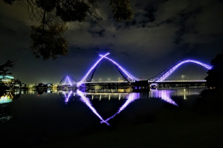 Illuminated bridge with purple lights reflected on a calm river at night.