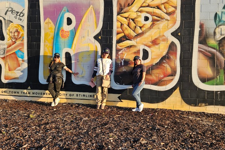 Three people pose in front of a colorful mural with large painted letters.