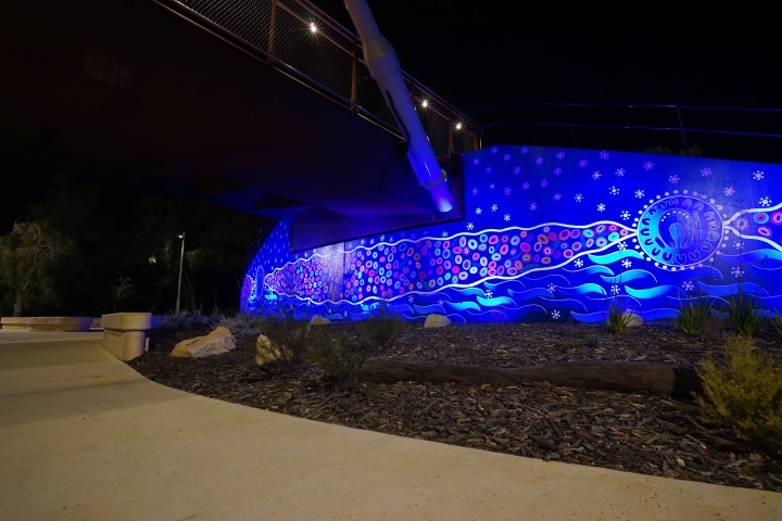 Colorful mural under a bridge illuminated at night, featuring abstract patterns and a circular design.