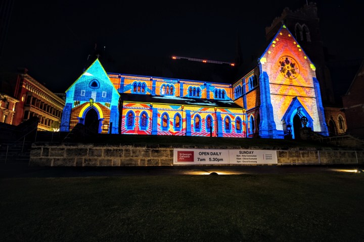 Church facade illuminated with colorful light projections at night.