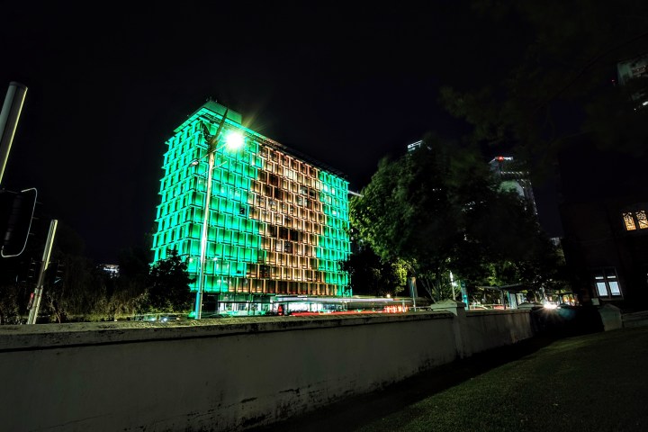 Night view of a building lit with green lights, featuring a central illuminated pattern.