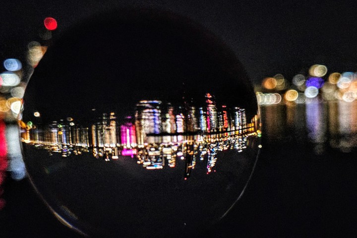 City skyline at night reflected in a glass sphere, with bokeh lights in the background.