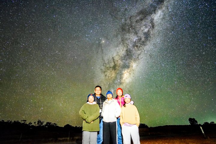 Six people standing under a starry night sky with the Milky Way visible.