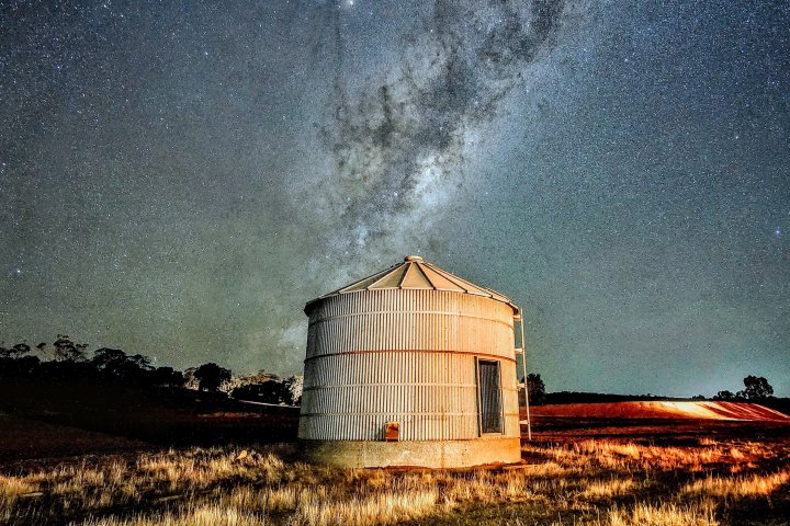 Grain silo under starry sky with Milky Way visible above.